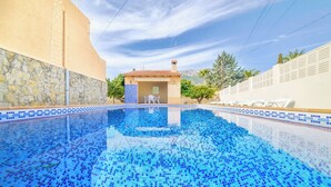 Una piscina con piastrelle blu a mosaico, un muro in pietra e un edificio con tetto in tegole.