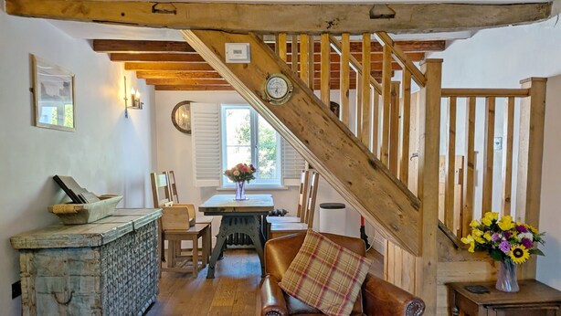 A rustic interior with a wooden staircase, a dining area with a table and chairs, and a seating area with a leather chair. - Springwell , West Wittering -  a cottage that sleeps 4 guests  in 2 bedrooms (Chichester)