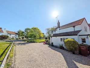 A rural setting with a gravel driveway leading to a white building with a red roof, surrounded by greenery and a clear sky.