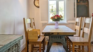 A dining area with a table, chairs, a vase with flowers, a clock, and a window with shutters. - Springwell , West Wittering -  a cottage that sleeps 4 guests  in 2 bedrooms (Chichester)