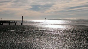 A beach with a pier extending into the water, a lighthouse in the distance, and a calm sea reflecting the sky. - Springwell , West Wittering -  a cottage that sleeps 4 guests  in 2 bedrooms (Chichester)