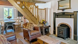 A living room with a fireplace, a wooden staircase, a leather armchair, and a table with a vase of flowers. - Springwell , West Wittering -  a cottage that sleeps 4 guests  in 2 bedrooms (Chichester)