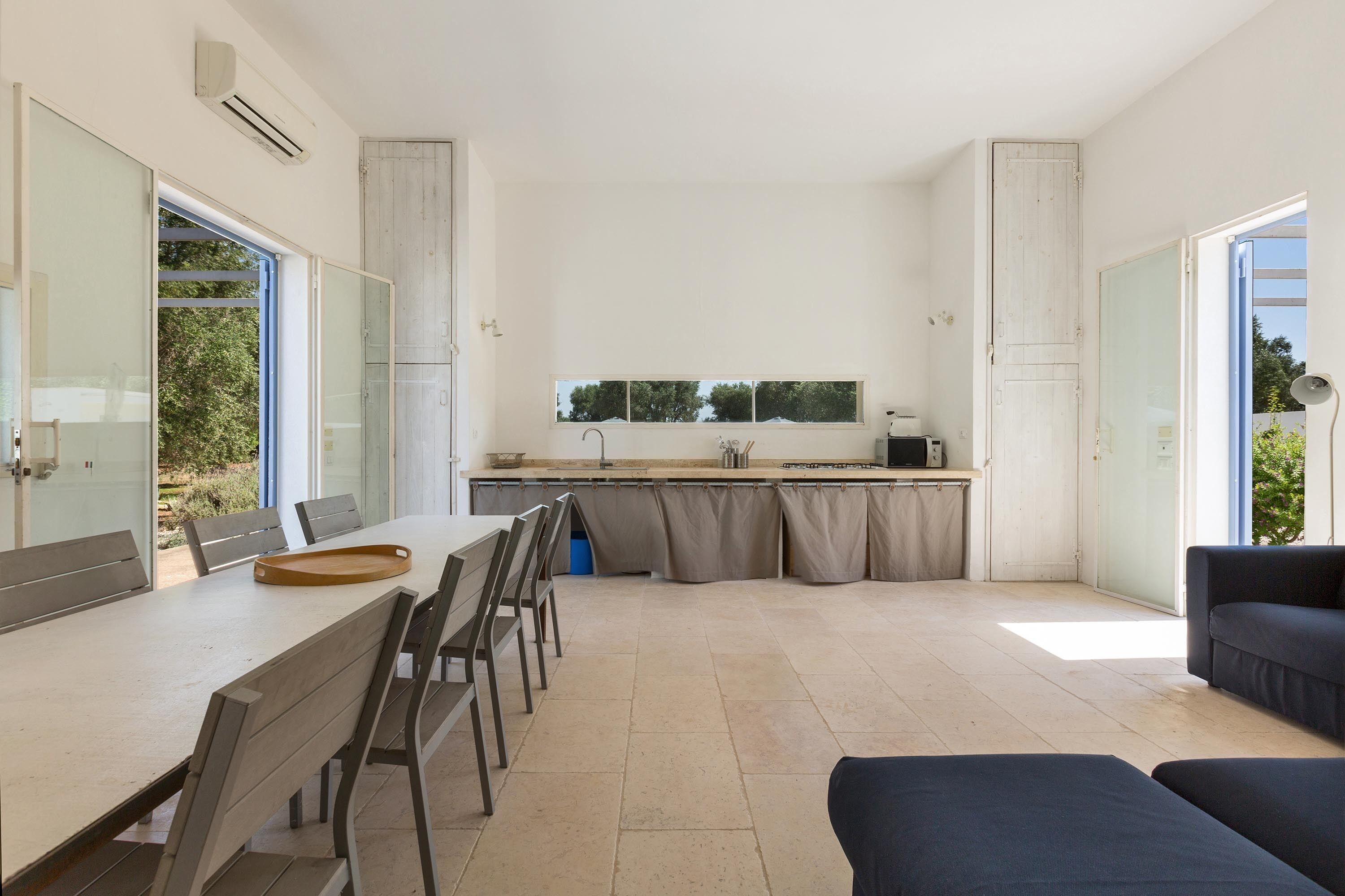 A modern kitchen with a large window, a dining area with a table and chairs, and a dark-colored sofa.