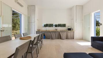A modern kitchen with a large window, a dining area with a table and chairs, and a dark-colored sofa.