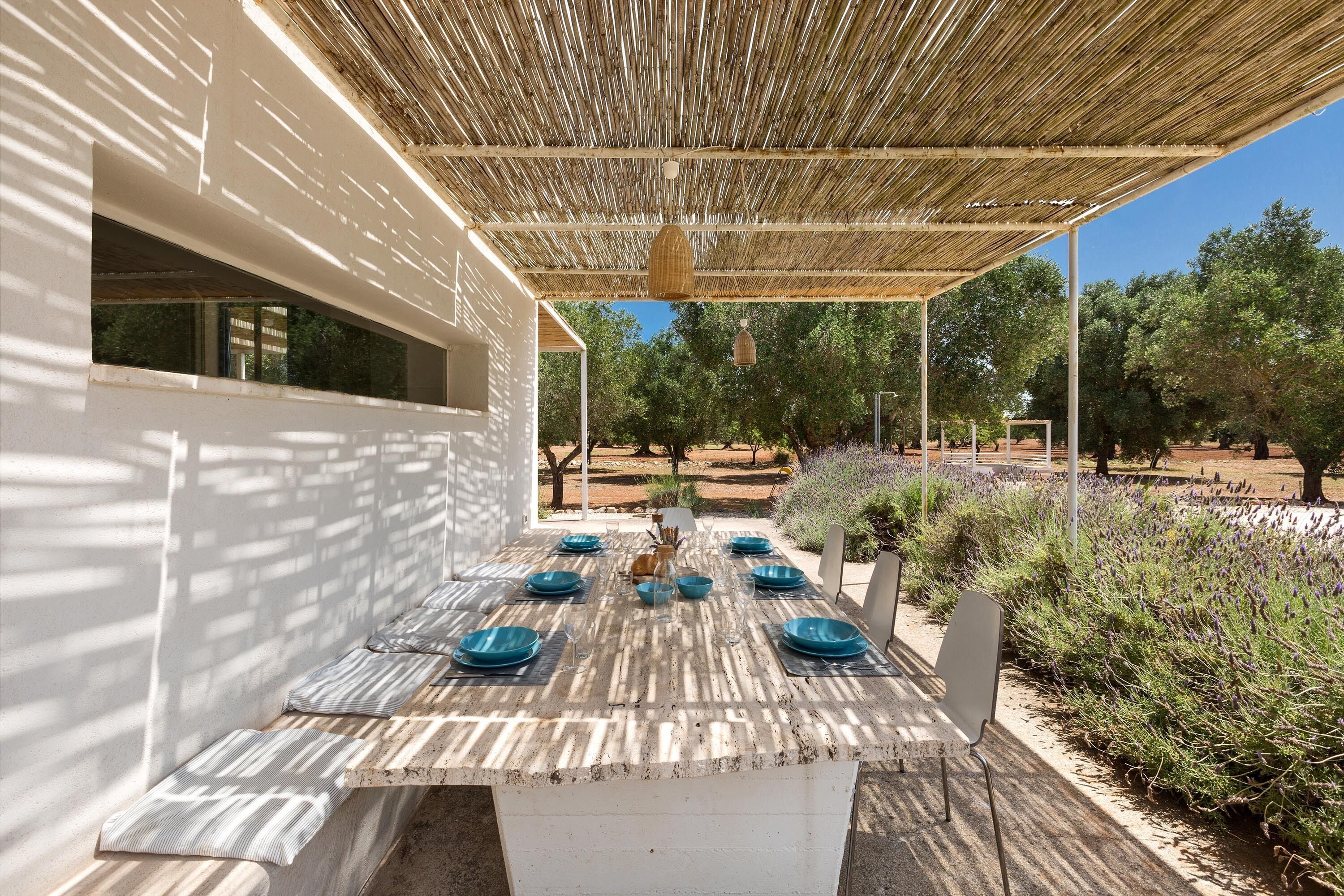 An outdoor dining area with a rustic wooden table, blue plates, and a woven canopy.