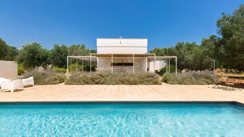 A swimming pool with a modern outdoor seating area and a building in the background.