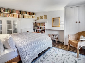 A bedroom with a bed, a bookshelf, a chair, a mirror, and a wardrobe.