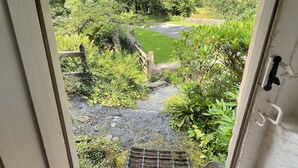 A view through a door of a garden with a gravel path, a wooden fence, and lush greenery. - Ball Cottage, Winsford (Winsford)