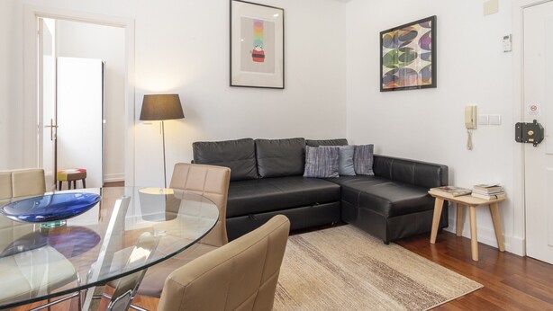 A modern living room with a glass dining table, a black leather sofa, and a small wooden side table. - Central Chiado Flat with Elevator CH6 by LV Premier (Lisboa ciudad)