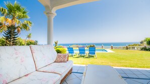 Un área de estar al aire libre cubierta con piscina, palmeras y vista al océano.