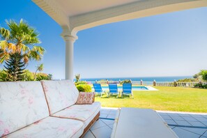 A covered outdoor seating area with a pool, palm trees, and a view of the ocean. - Cubo's Villa Las Colinas / Private pool / wifi / air conditioning (Benalmádena)