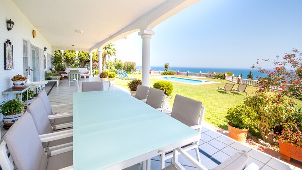 Un patio techado con piscina, mobiliario exterior y vista al océano.