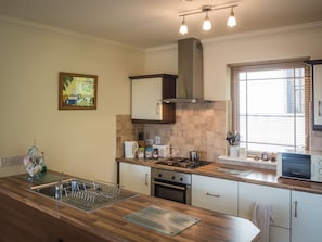 A kitchen with a stove, oven, sink, and a window with blinds.