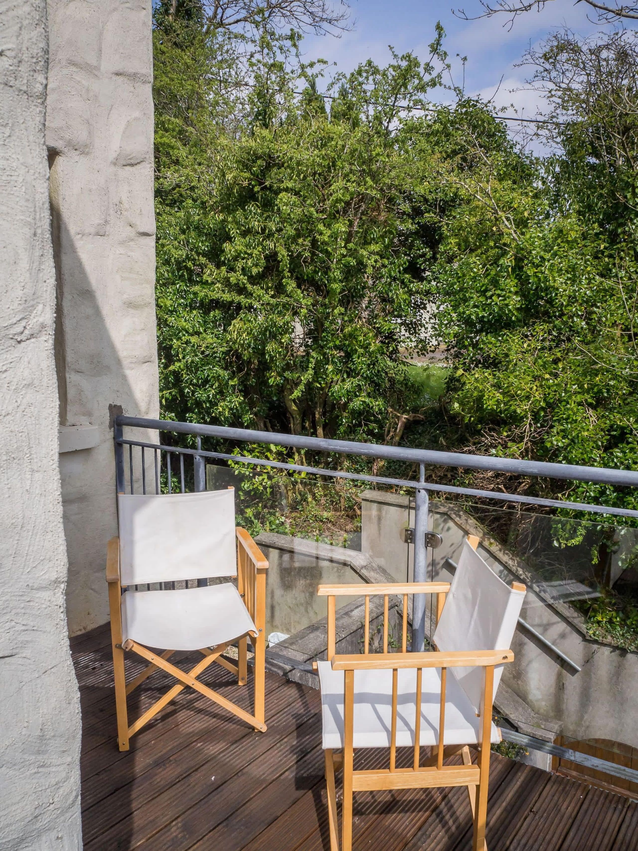Two white cushioned chairs on a wooden deck with a metal railing, overlooking a lush green landscape.