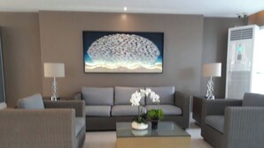 Un salon moderne avec un canapé gris, deux fauteuils, une table basse ornée de fleurs blanches et un grand tableau abstrait accroché au mur.