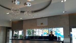 Un hall d’entrée moderne avec un comptoir d’accueil, des lustres et de grandes fenêtres offrant une vue dégagée.