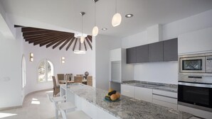 Une cuisine moderne dotée d’un plan de travail en granit, d’appareils électroménagers en acier inoxydable et de luminaires suspendus.