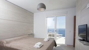 Une chambre moderne avec un grand lit, une télévision et une vue sur la mer, accessible par une porte-fenêtre coulissante.