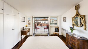 A bedroom with a bed, a desk, a chair, a dresser, and a large window with a view of buildings. - Ca' Cerchieri Terrace Canal View (Venice)