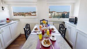 A breakfast setup with a table, chairs, and a view of buildings through large windows. - Ca' Cerchieri Terrace Canal View (Venice)
