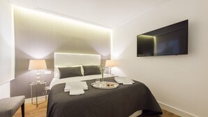 A modern hotel room with a large bed, bedside lamps, a flat-screen TV, and a tray with breakfast items.