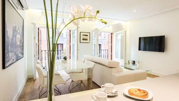 A modern living room with a glass coffee table, white sofas, and a dining area with a white table and chairs.