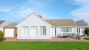 A single-story house with a white exterior, a brick garage, and a small front porch with a bench. - A family house that sleeps 6 guests  in 3 bedrooms (Chichester)
