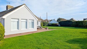 A white bungalow with a sloped roof, a small porch, and a well-maintained lawn. - A family house that sleeps 6 guests  in 3 bedrooms (Chichester)