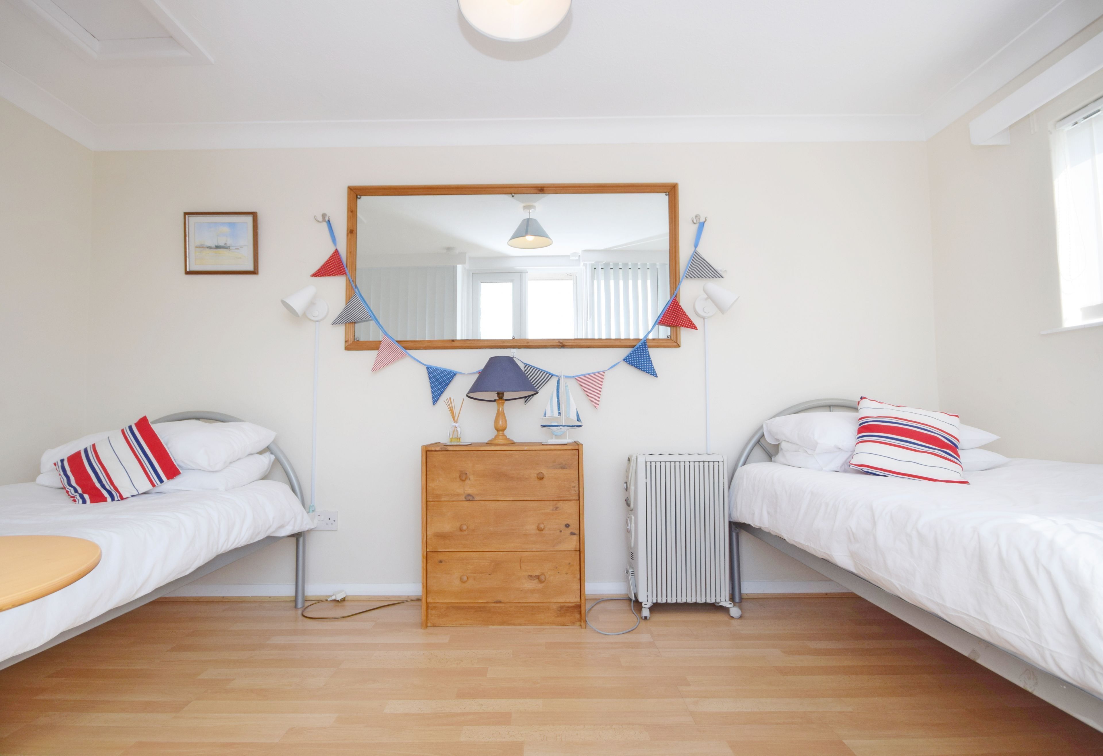 Une chambre avec deux lits simples, une commode en bois, un miroir et un radiateur.
