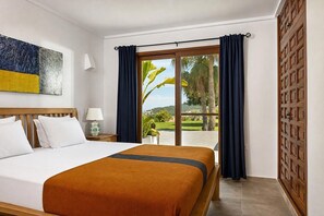 Ein Hotelzimmer mit einem Bett, einem Nachttisch, einer Lampe, Blick ins Freie und einer Holztür.