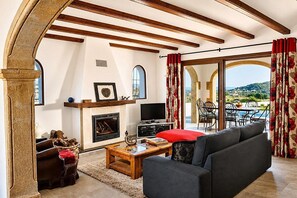 Ein Wohnzimmer mit Kamin, einer Couch und Blick ins Freie.