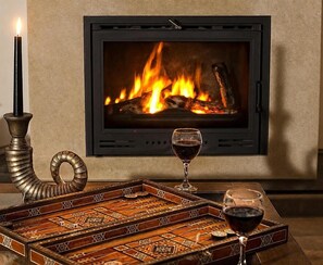 Ein Kamin mit Holzscheiten, eine Kerze und zwei Gläser Rotwein auf einem Tablett.