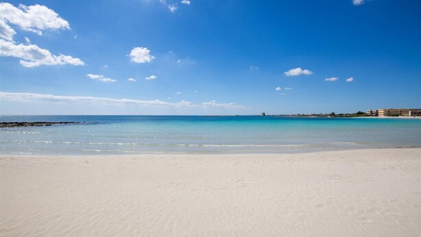 A wide sandy beach with clear turquoise waters and a few scattered clouds.