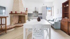 A modern kitchen with a brick fireplace, white cabinetry, and a dining area with a white table and chairs.