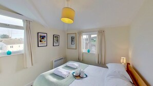 Een hotelkamer met een bed, twee ramen met gordijnen, een radiator en foto's in lijsten aan de muur.