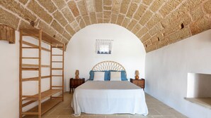 A bedroom with a stone ceiling, a bed with a striped bedspread, two nightstands with lamps, and a wooden ladder.
