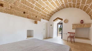 A room with a bed, a chair, a small table, a fireplace, and an arched ceiling.
