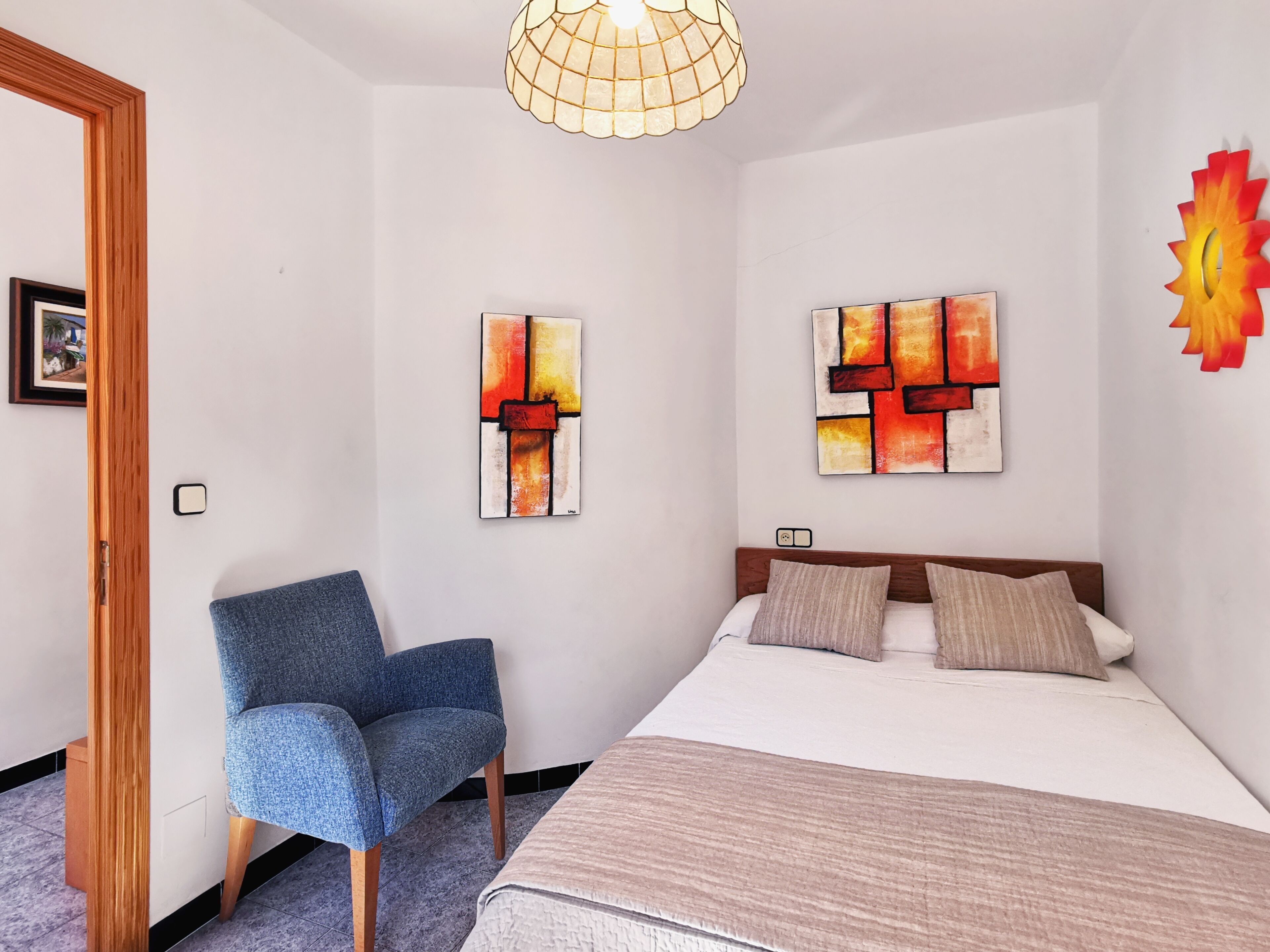 A bedroom with a bed, two pillows, a chair, and two abstract paintings on the wall.