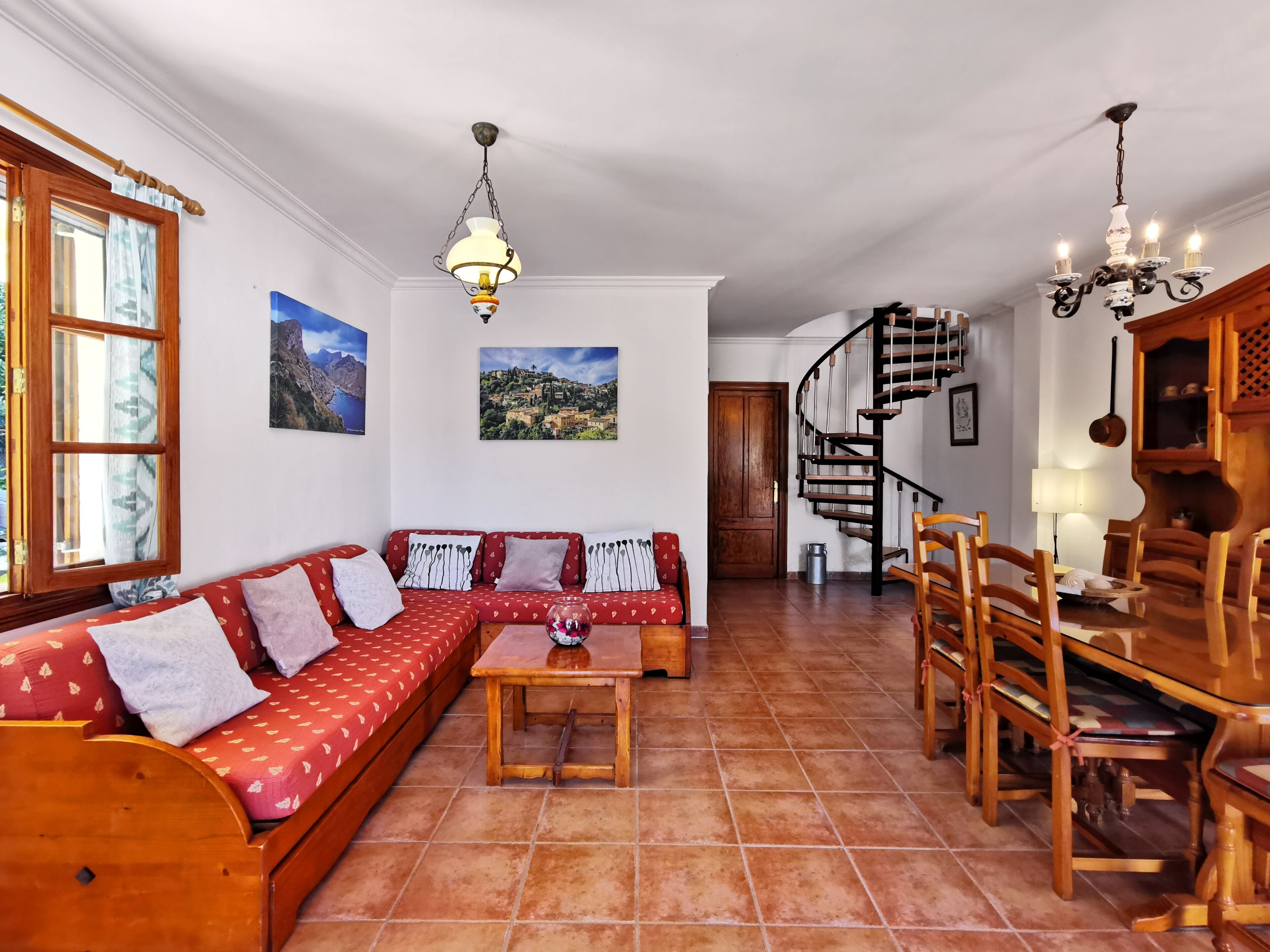 A spacious living room with a wooden sofa, a dining table, and a spiral staircase.