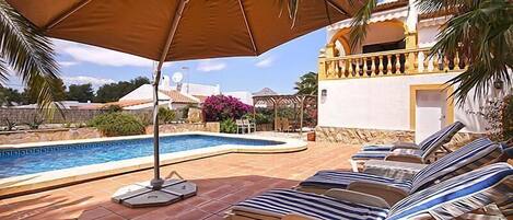 Un área de piscina con sillones de descanso y un parasol grande.
