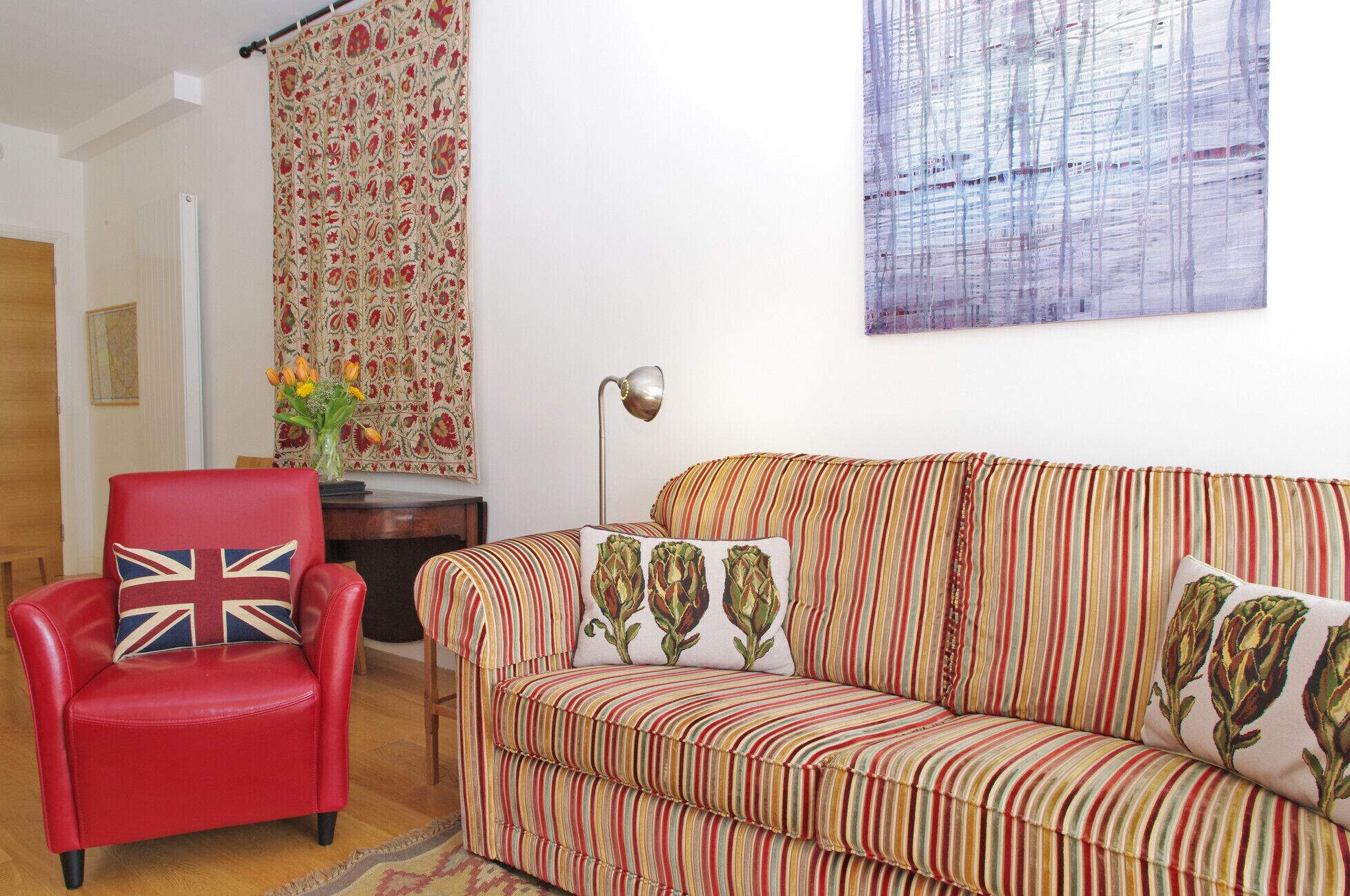 A living room with a red leather armchair, a striped sofa, a floral tapestry, and a modern lamp.