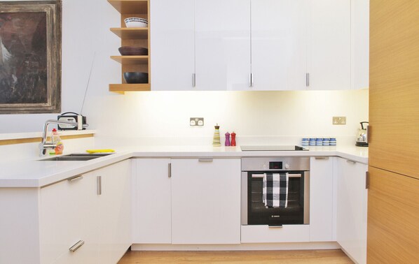 A modern kitchen with white cabinets, a Bosch dishwasher, and a wooden shelf above the counter.