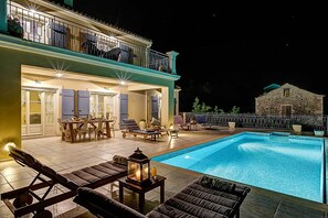 Zona de piscina con sillas de descanso, una mesa de comedor y un edificio de piedra al fondo.