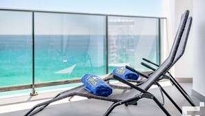 Ein Balkon mit zwei Liegestühlen und einem blauen Handtuch mit dem Schriftzug 'TURIS', mit Blick auf das klare, blaue Meer.