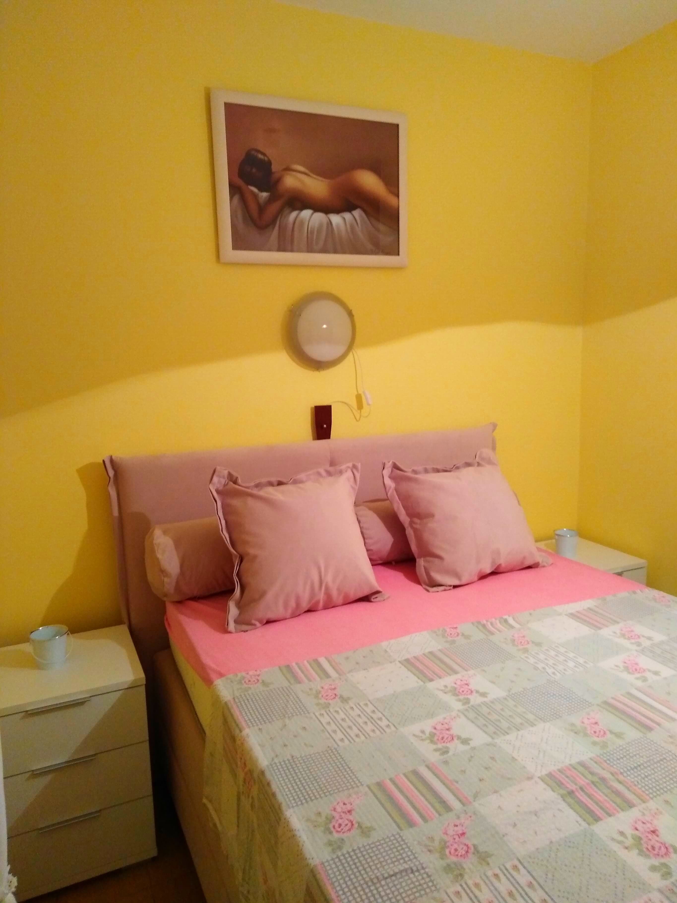 A bedroom with a bed, two bedside tables, a nightstand, a wall-mounted lamp, and a painting.