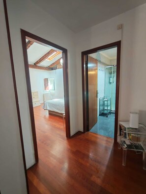 Ein Zimmer mit Holzboden, einem Bett, einem Fenster und einer Tür zu einem Badezimmer mit Dusche.
