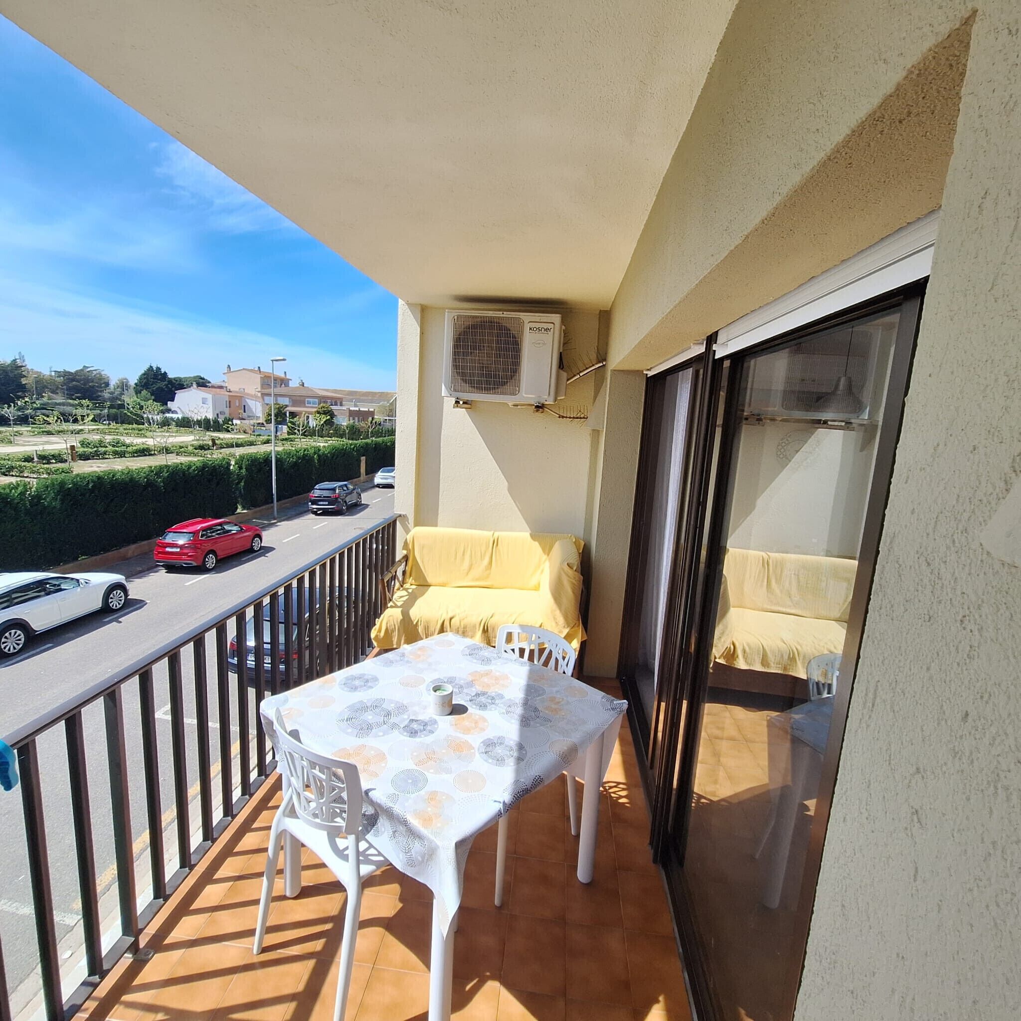 Un balcone con tavolo e sedie, un divano, un condizionatore d'aria e vista su una strada con auto.