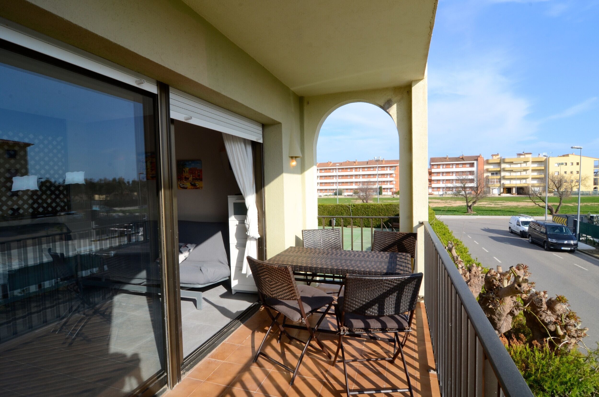A balcony with a table and chairs, a sliding glass door, and a view of a street and buildings.