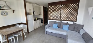Um espaço compacto com cozinha americana, uma mesa de jantar com cadeiras e um sofá com almofadas.