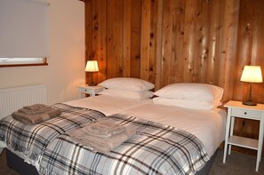A double bed with plaid bedding, two bedside tables with lamps, and a wooden wall.